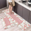 A set of two pink and white diamond print non-slip kitchen rugs placed on a light wood floor next to dark cabinets.
