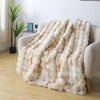 A beige luxury faux rabbit fur throw blanket draped over a light-colored sofa.