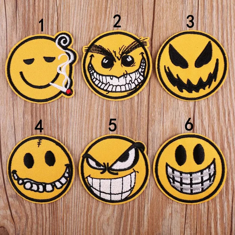 Six embroidered patches showing various angry and menacing emoji faces on a wooden background.