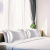 White silky satin pillowcases on a bed with sheer curtains and natural light.