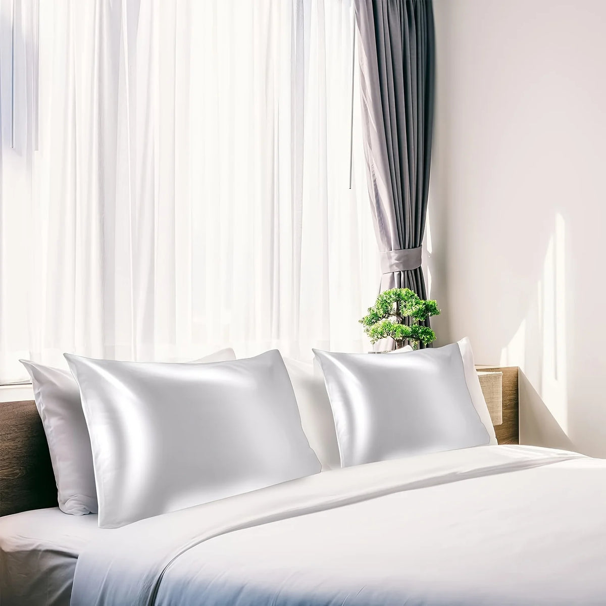 White silky satin pillowcases on a bed with sheer curtains and natural light.