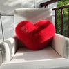 A bright red heart-shaped fox fur throw pillow resting on a light-colored outdoor chair.