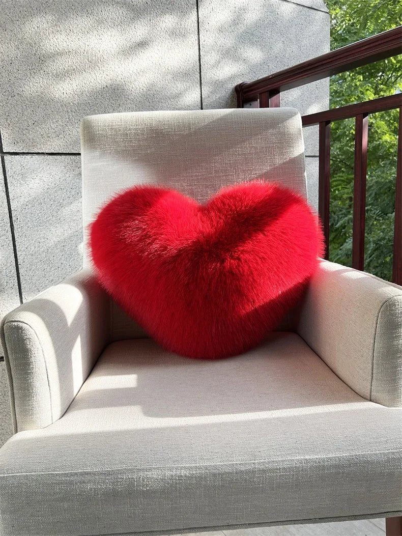A bright red heart-shaped fox fur throw pillow resting on a light-colored outdoor chair.
