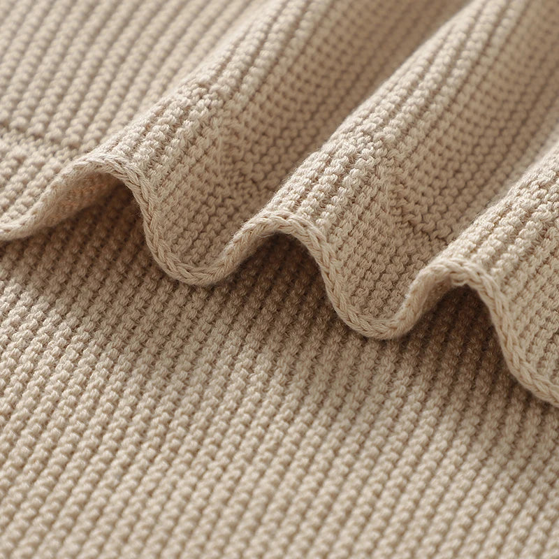 A beige cotton baby swaddle blanket folded and draped, showing a textured knit fabric.