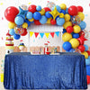 A blue sequin rectangle table cover is displayed in front of a backdrop of colorful balloons and a white wooden structure.