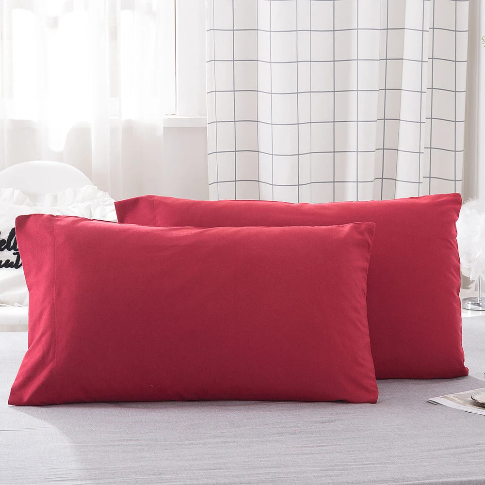 Two solid red microfiber pillow covers resting on a light gray bed with a white checkered curtain in the background.