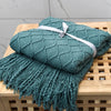 A teal knitted tassel throw blanket folded on a wooden surface.