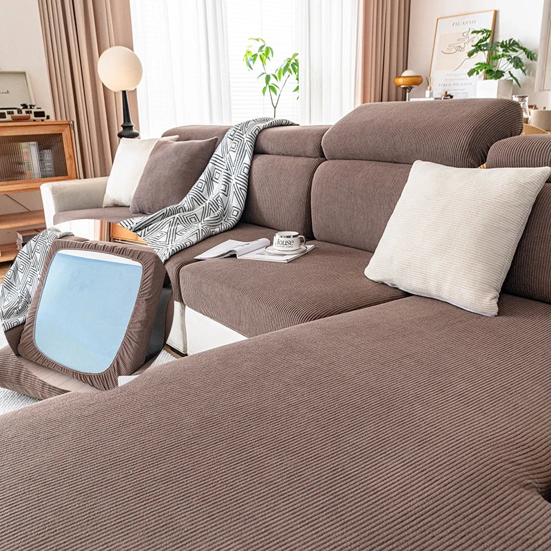 A plush, ribbed brown sofa cushion cover with light gray throw and pillows on a modern sofa.