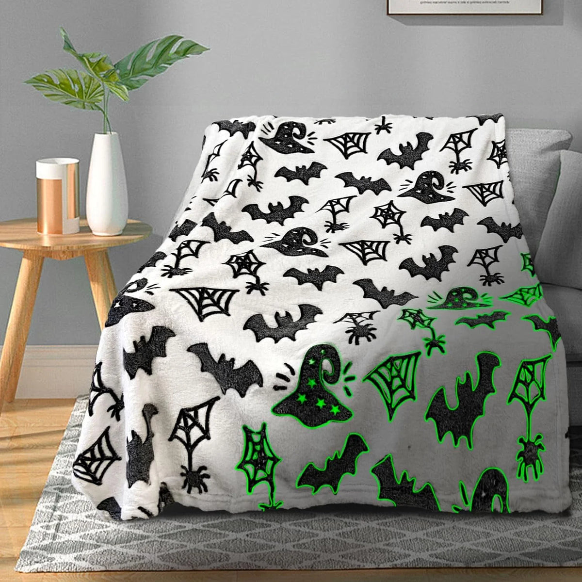 A black and white glow-in-the-dark bat and spider print coral fleece blanket displayed on a gray rug.