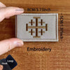 A close-up of a beige embroidered patch featuring a cross design on a wooden surface.