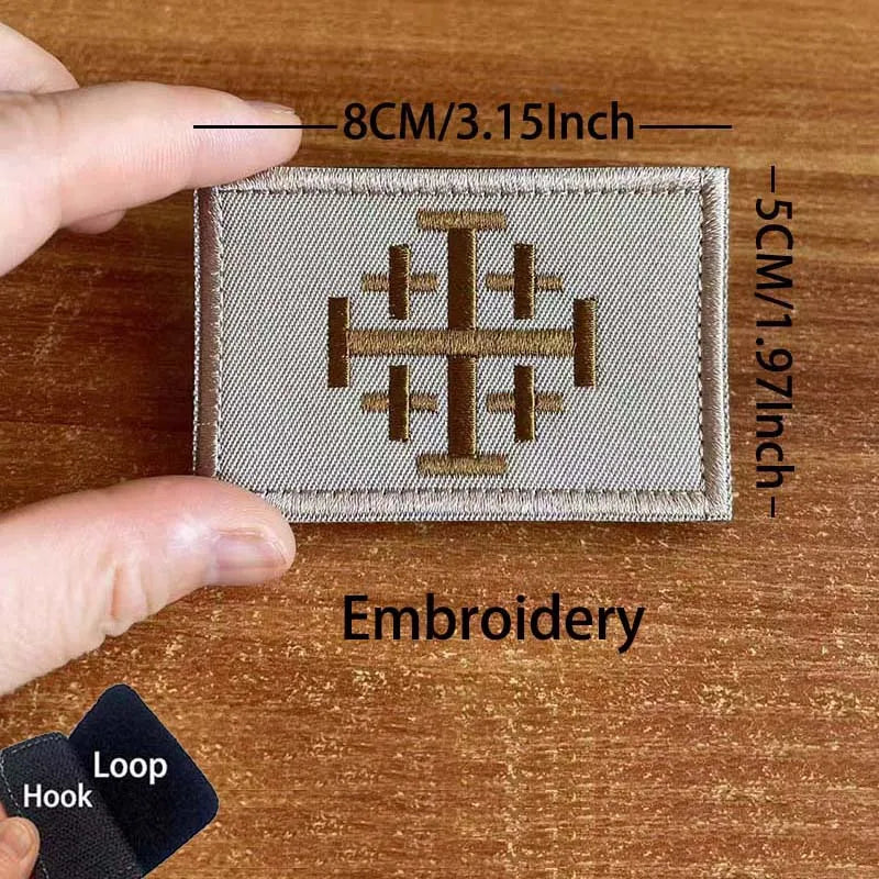 A close-up of a beige embroidered patch featuring a cross design on a wooden surface.