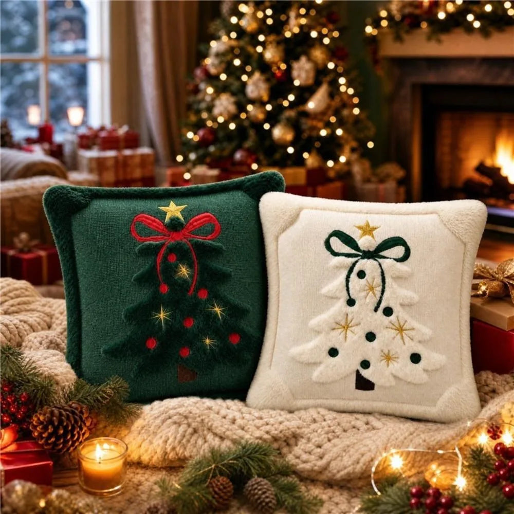 Two embroidered Christmas tree velvet pillows resting on a knitted surface near a decorated fireplace.