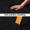 A hand is touching a black plush rug, showing the soft and non-shedding texture.