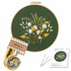 Embroidery DIY kit featuring a green fabric with yellow and white floral embroidery designs and a spool of embroidery thread