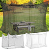 A large outdoor mosquito netting draped over a wooden table and bench in a grassy outdoor setting.
