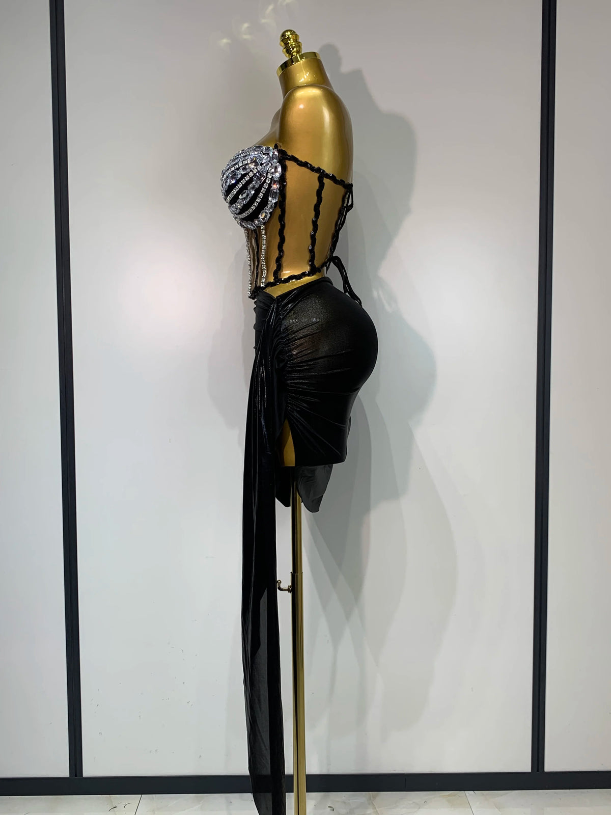 A black performance set displayed on a gold mannequin with dangling silver beads.