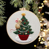 A hand embroidery kit featuring a small, fluffy mouse nestled in a festive Christmas tree design.