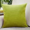 A square olive green velvet cushion cover resting on a light-colored sofa.