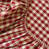 A close-up of a red and cream gingham fabric gathered at the hem, showing soft folds and texture.