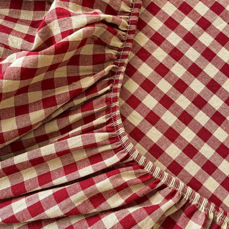 A close-up of a red and cream gingham fabric gathered at the hem, showing soft folds and texture.
