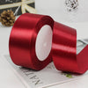 A roll of deep red satin ribbon with a white center core lying on a piece of paper.