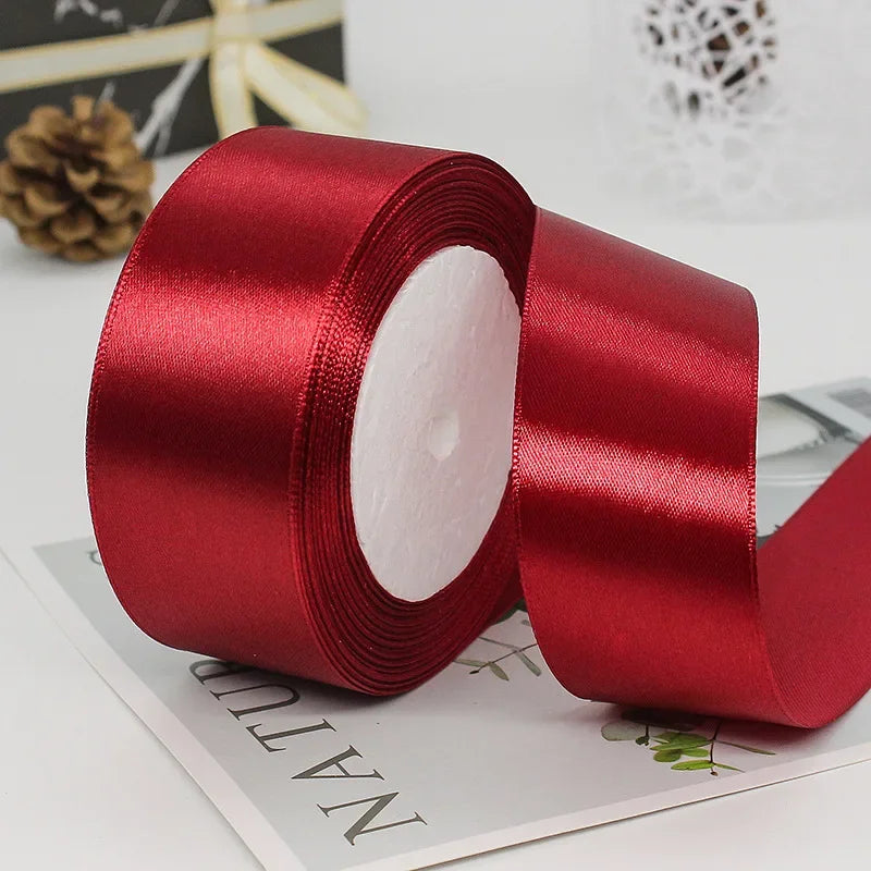 A roll of deep red satin ribbon with a white center core lying on a piece of paper.