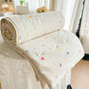 A cream-colored quilt blanket with colorful scattered stars and hearts rolled up on a white bed.