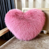 A fluffy pink heart-shaped fox fur throw pillow resting on a wooden surface.