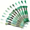 A collection of twelve threads of rainbow gradient embroidery floss in various shades are displayed with a green gradient bac