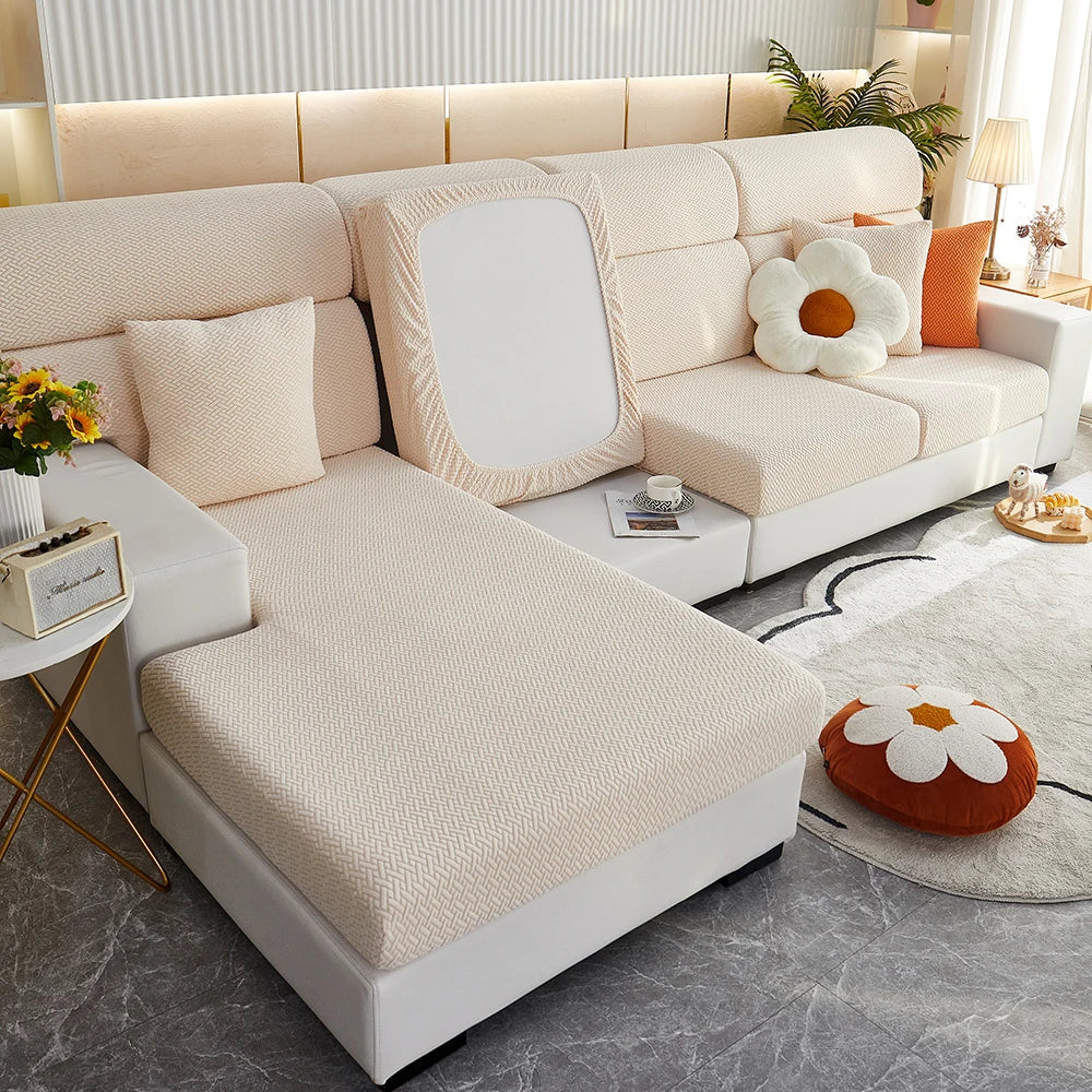 A modern beige Jacquard sofa slipcover with elastic edges featuring light wood accents and orange pillows.