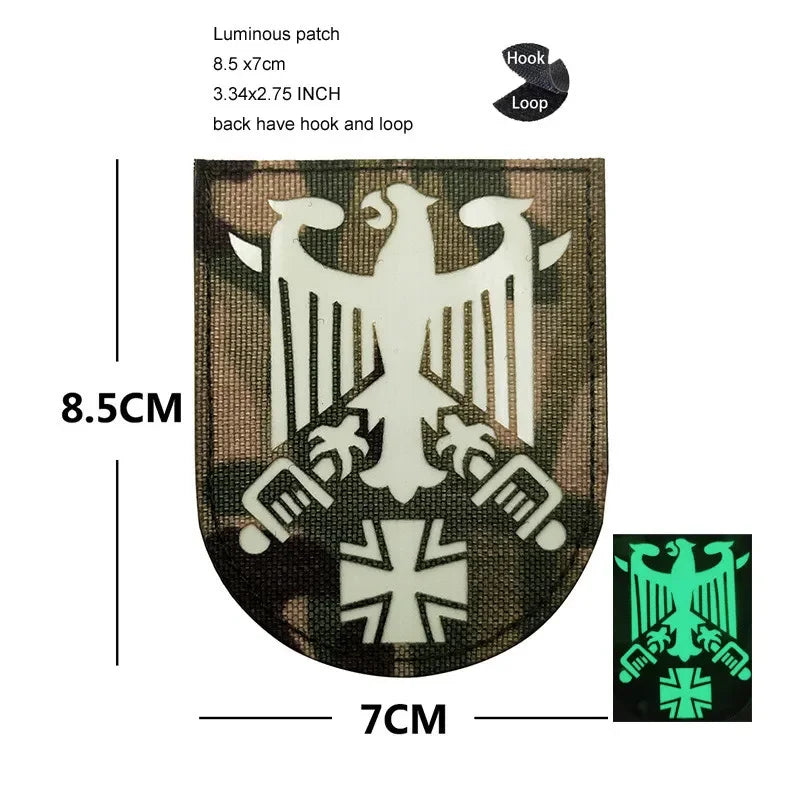 A dark brown luminous patch featuring a white eagle shield design with a black border and hook and loop attachment.