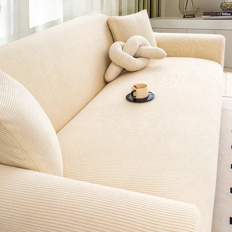 A cream-colored stretch jacquard sofa slipcover with a textured fabric and a neutral throw pillow.