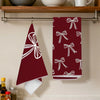 A set of two deep red kitchen towels featuring white bow patterns hanging on a metal rack.