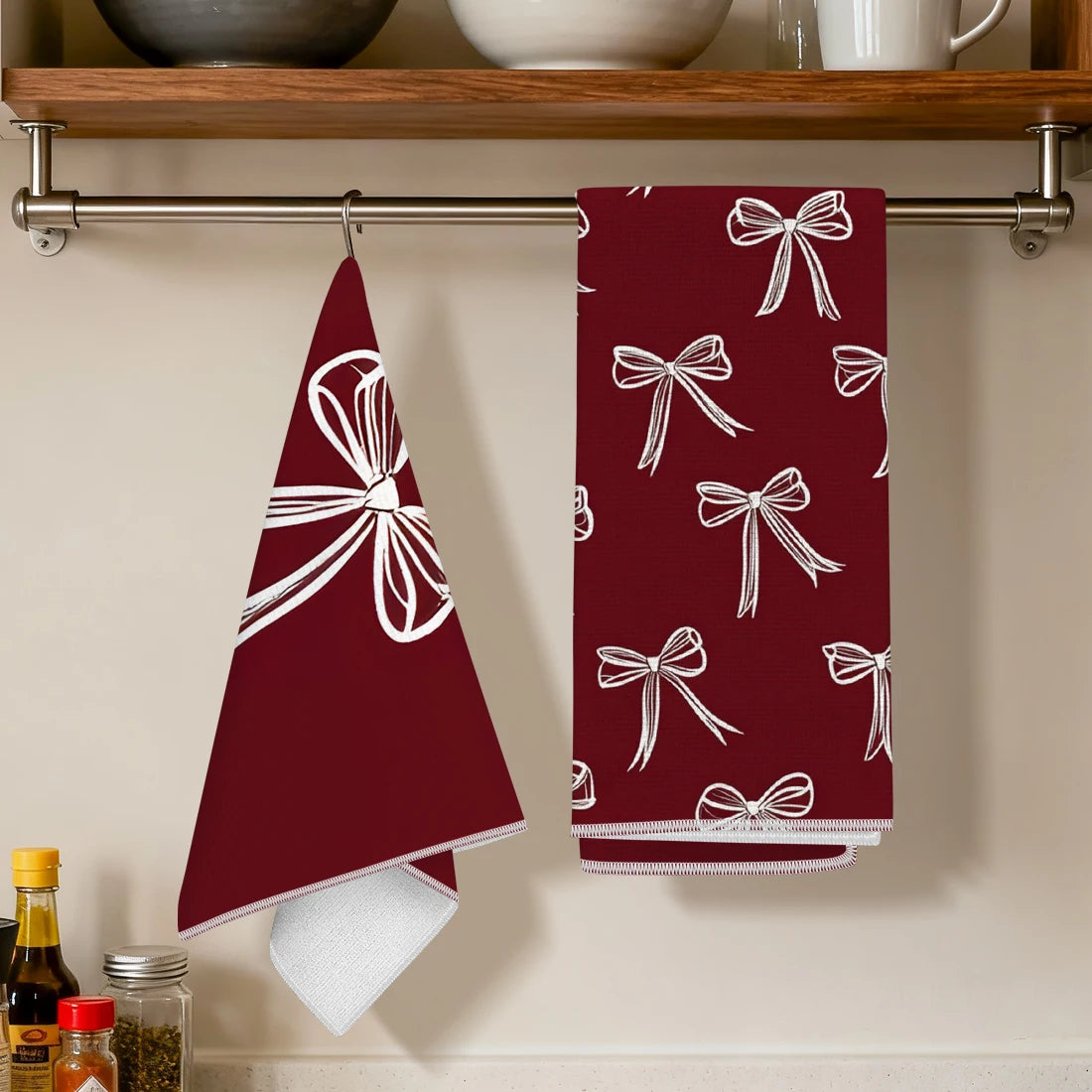 A set of two deep red kitchen towels featuring white bow patterns hanging on a metal rack.