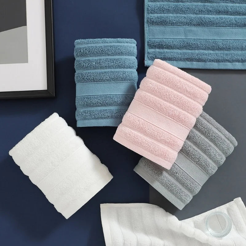 A set of four soft, striped face towels in light blue, pink, and gray are displayed on a dark surface.