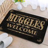 A black entrance mat with gold lettering that reads MUGGLES WELCOME on a light wooden surface.