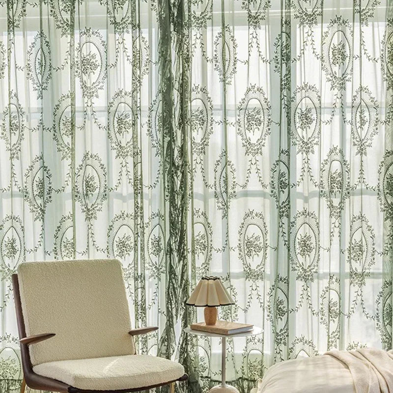 Sheer floral lace curtain panels with green and white patterns covering a window.