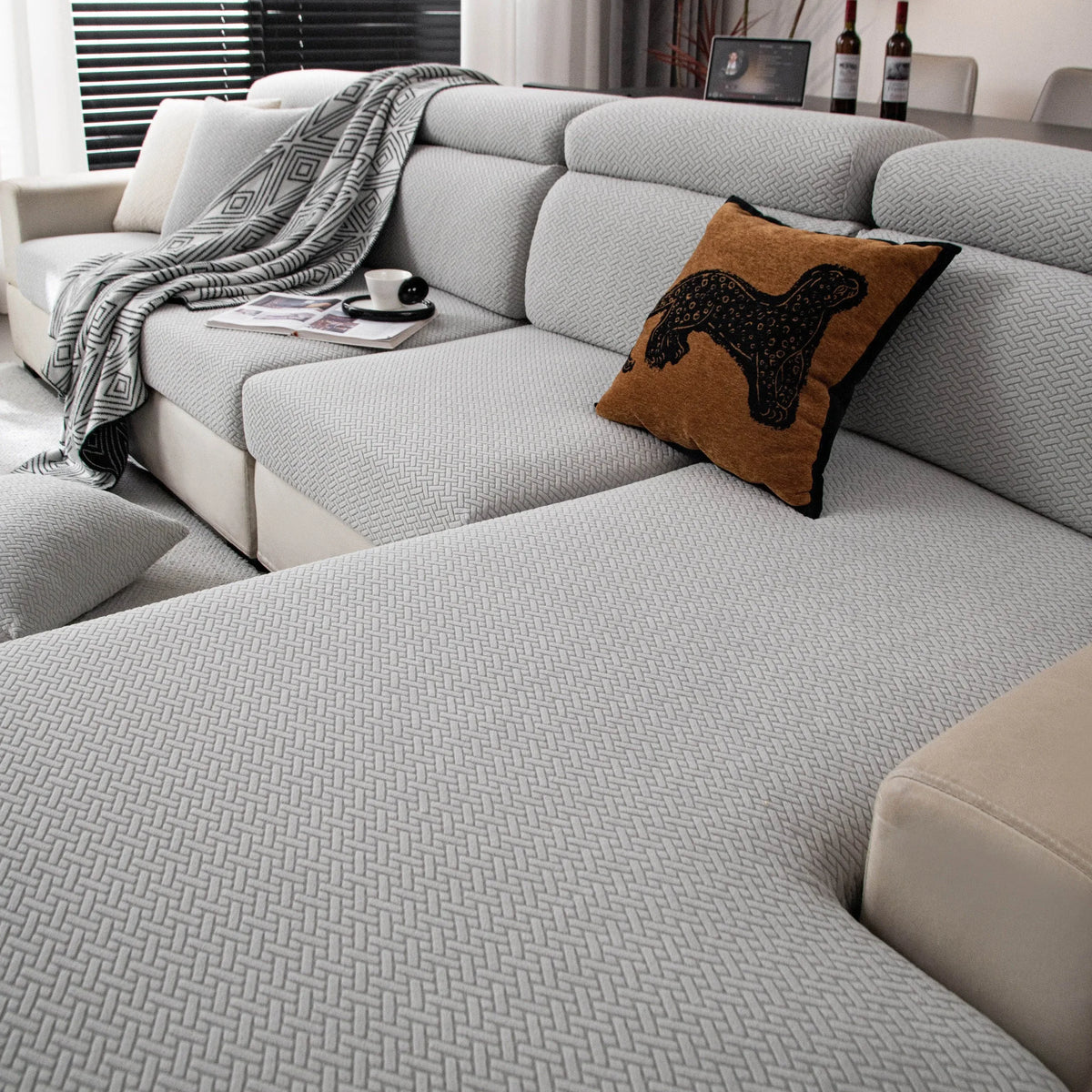 A light gray stretchy polar fleece sofa cover with a dark brown decorative pillow and a gray throw blanket on a modern sofa.