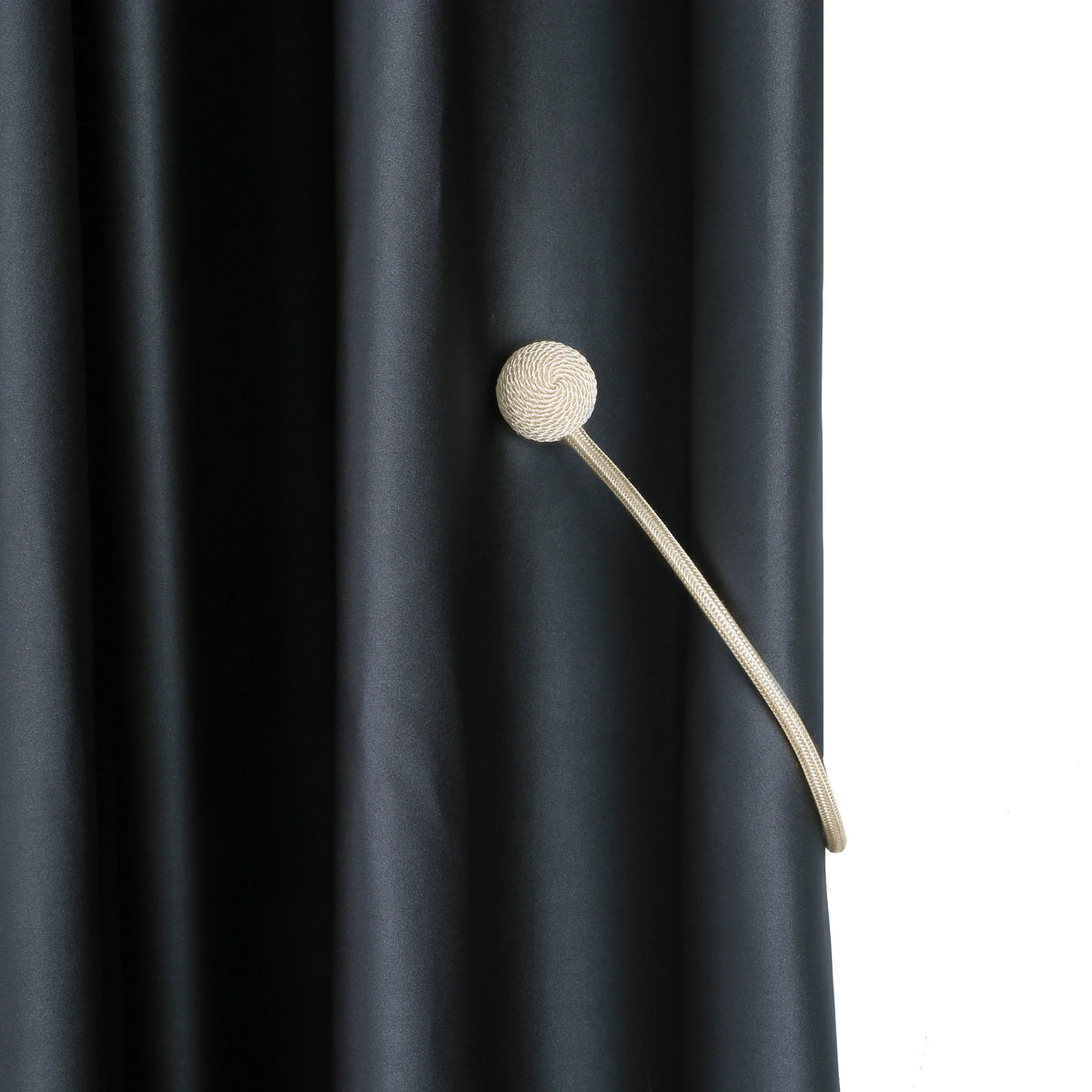 A close-up of a beige magnetic curtain tieback attached to a dark gray fabric curtain.