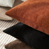A stack of three throw pillows in shades of rust brown, black, and dark olive green linen texture.