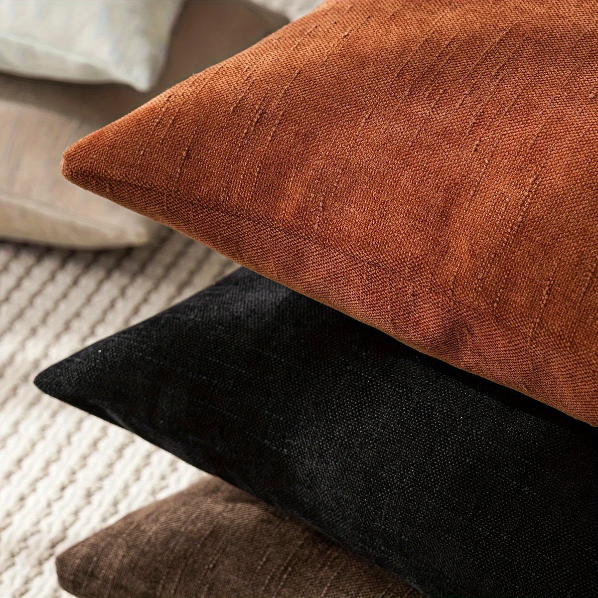 A stack of three throw pillows in shades of rust brown, black, and dark olive green linen texture.