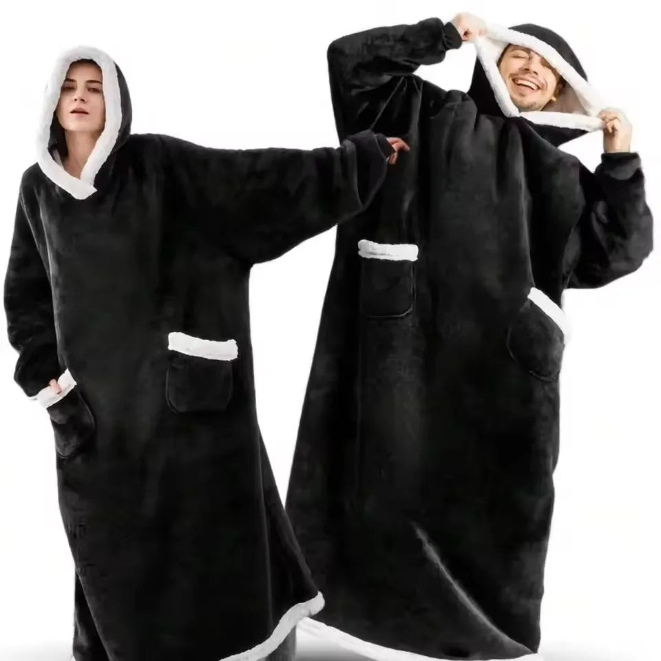 A person wearing an oversized black flannel blanket pyjama set, with the hood pulled up and a smiling face visible.