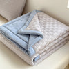 A stack of light blue and gray breathable waffle quilts folded on a white surface.
