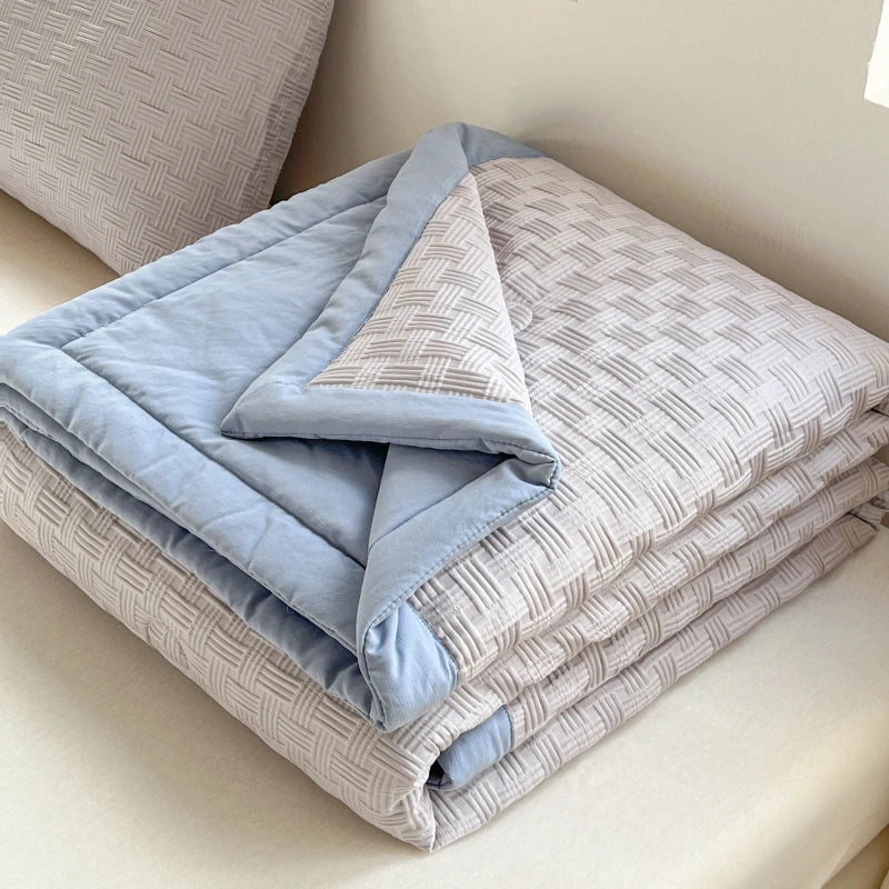 A stack of light blue and gray breathable waffle quilts folded on a white surface.