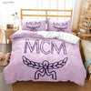 Pink duvet cover set featuring a large embroidered MCM logo and a stylized winged design on a bed.