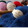 A close-up of a hand-knitted blue wool scarf featuring a white label that reads Wool Thread Delicate and Soft Intimate Warmth