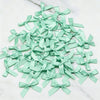 A pile of light mint green satin ribbon bows scattered on a white marble surface.