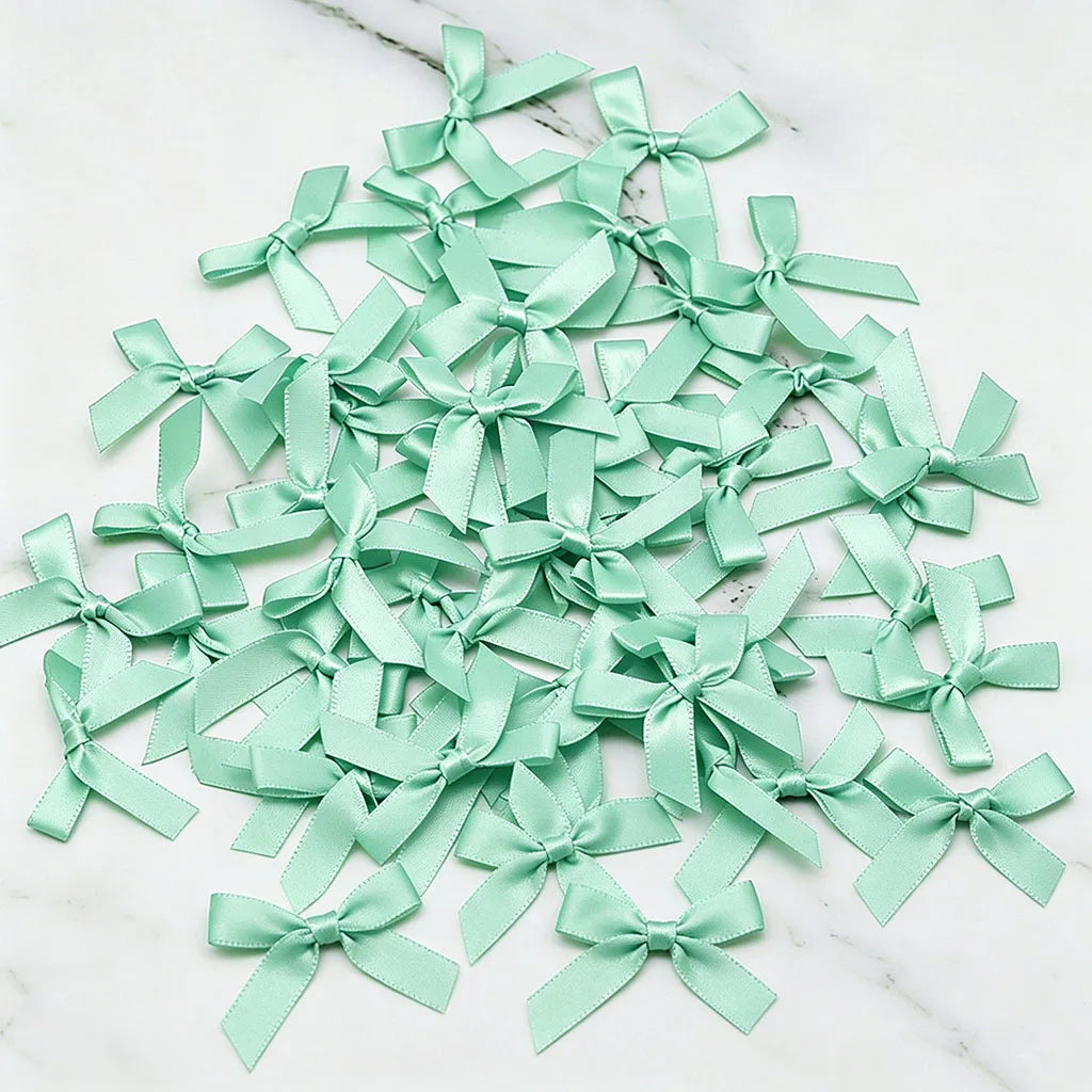A pile of light mint green satin ribbon bows scattered on a white marble surface.
