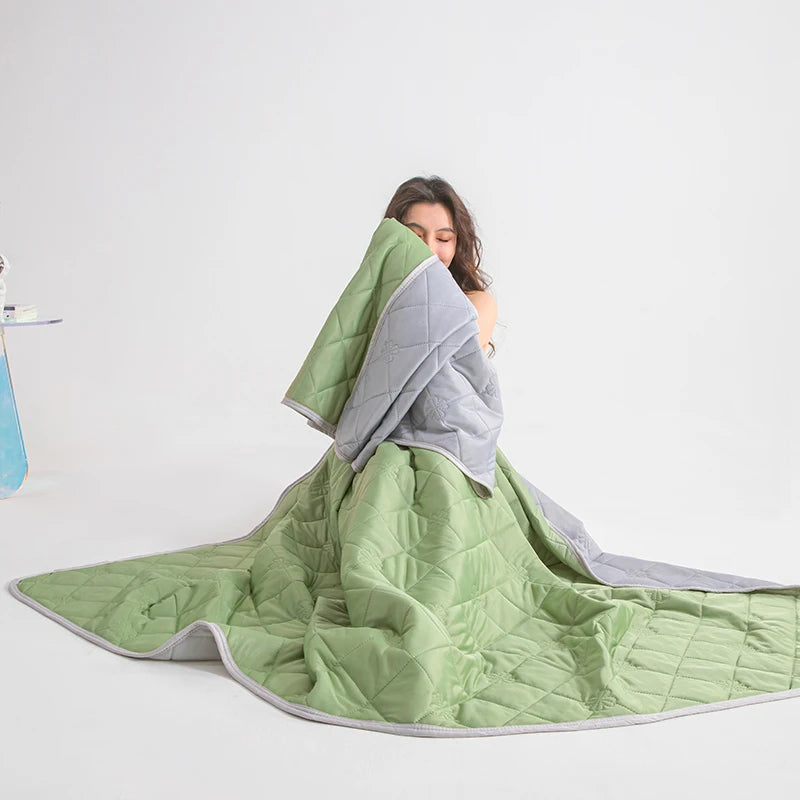 A person is looking at a light green quilted blanket draped over their shoulder.