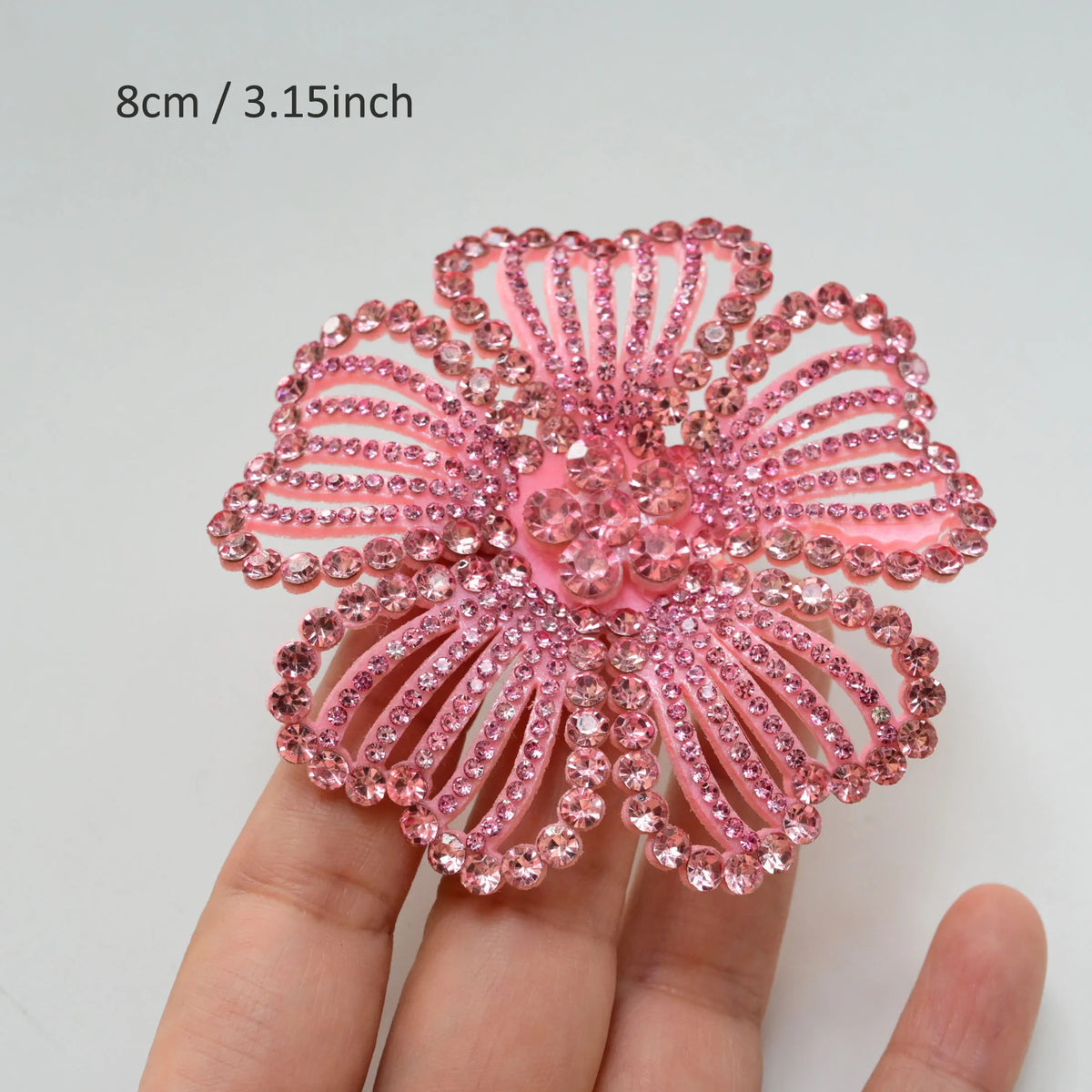 A close-up of a pink rhinestone flower applique patch for clothing being held in a hand.